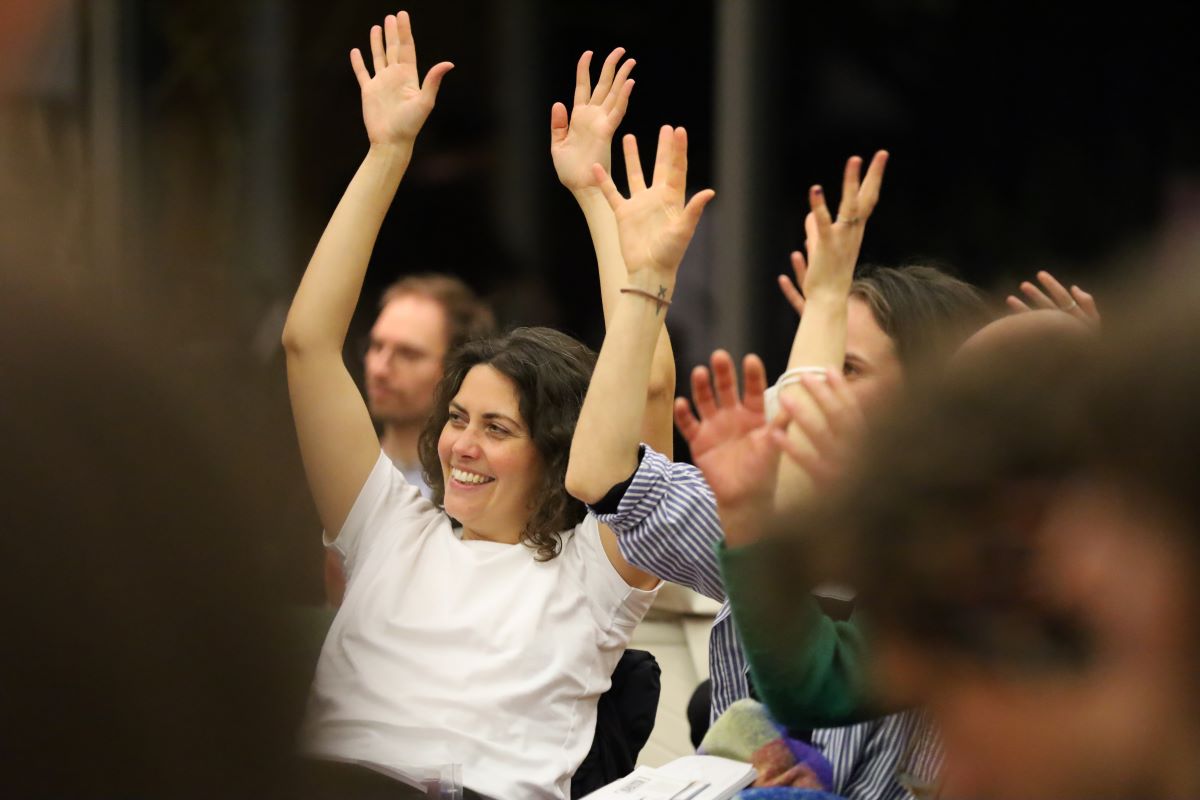 Teilnehmerinnen einer Konferenz halten die Hände in die Höhe.