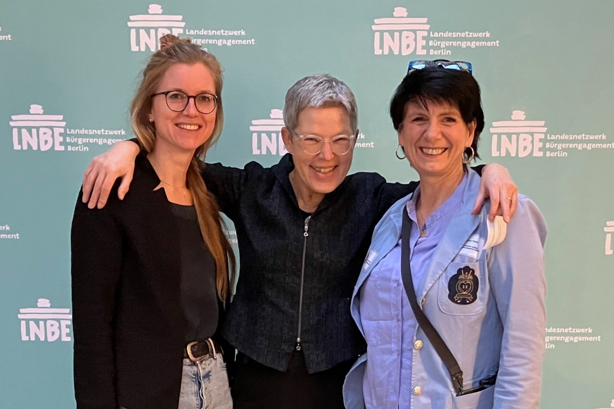 Drei Frauen die vor der Logowand des Landesnetzwerks Bürgerengagement Berlin stehen.