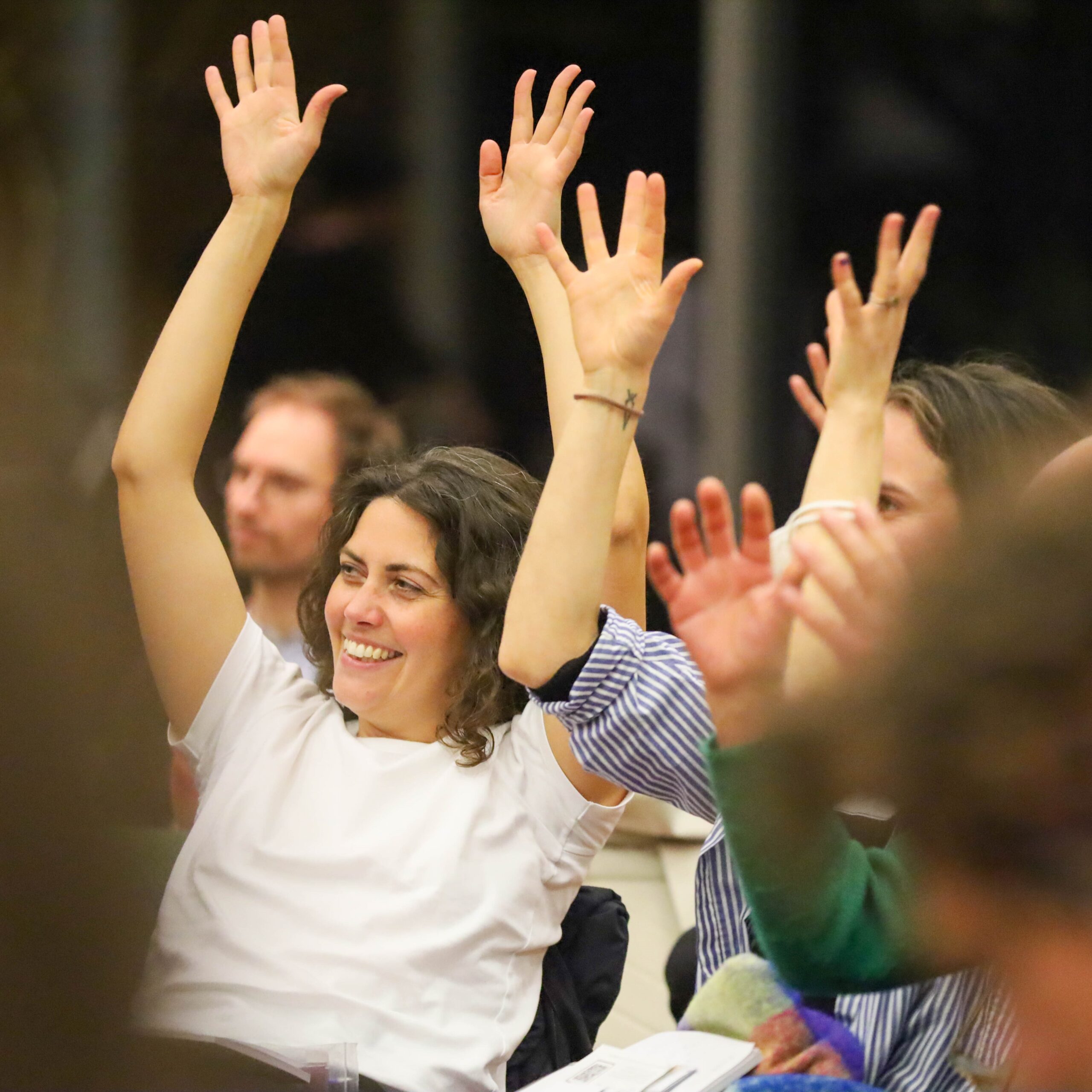 Teilnehmer:innen halten die Hände bei einer Konferenz in die Höhe.