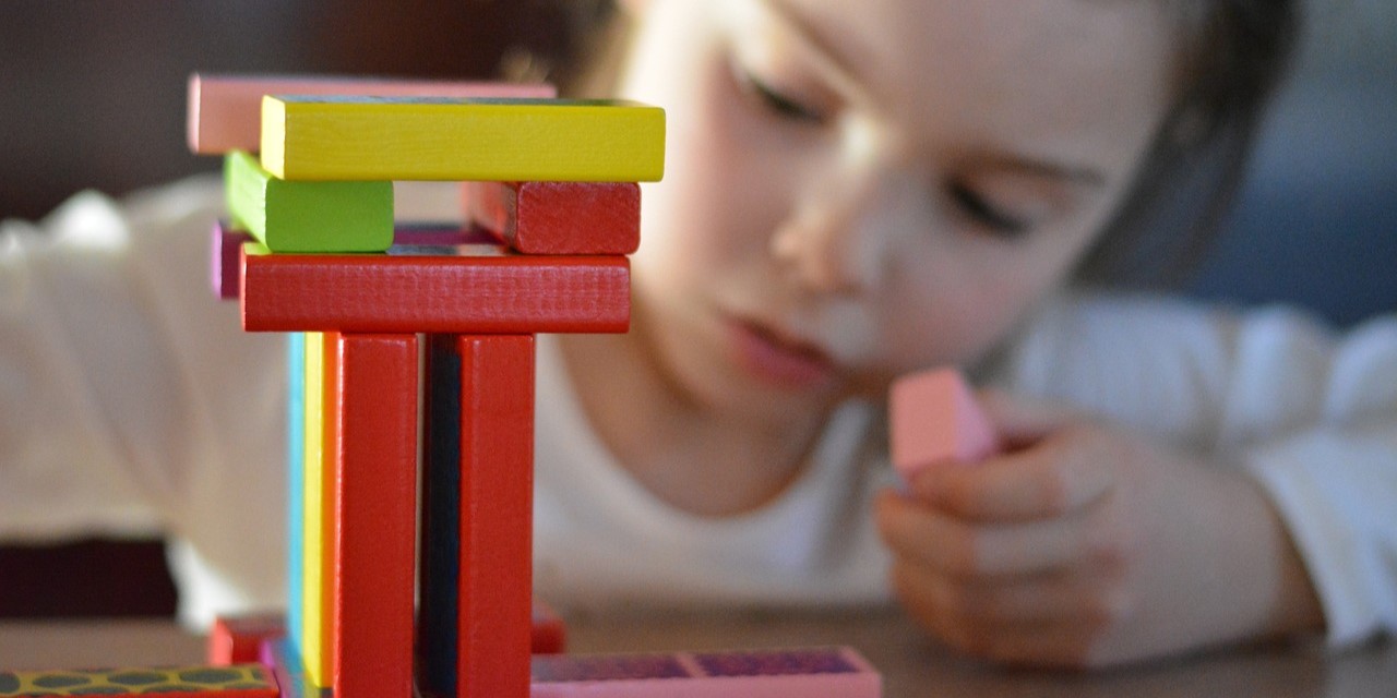 Ein spielendes Kind, das einen Turm mit bunten Holzklötzen baut.