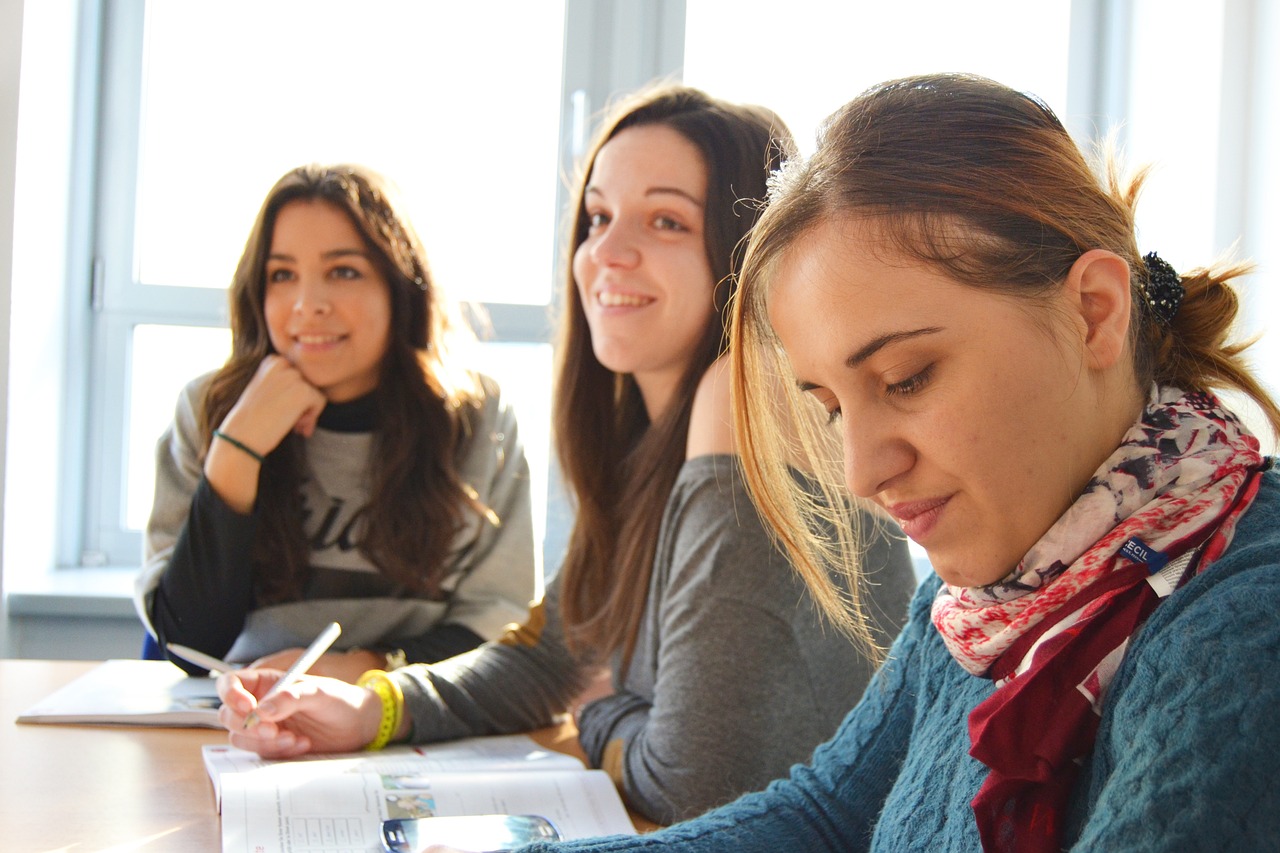 Drei junge Frauen sitzen an einem Tisch und hören bei einer Veranstaltung zu.