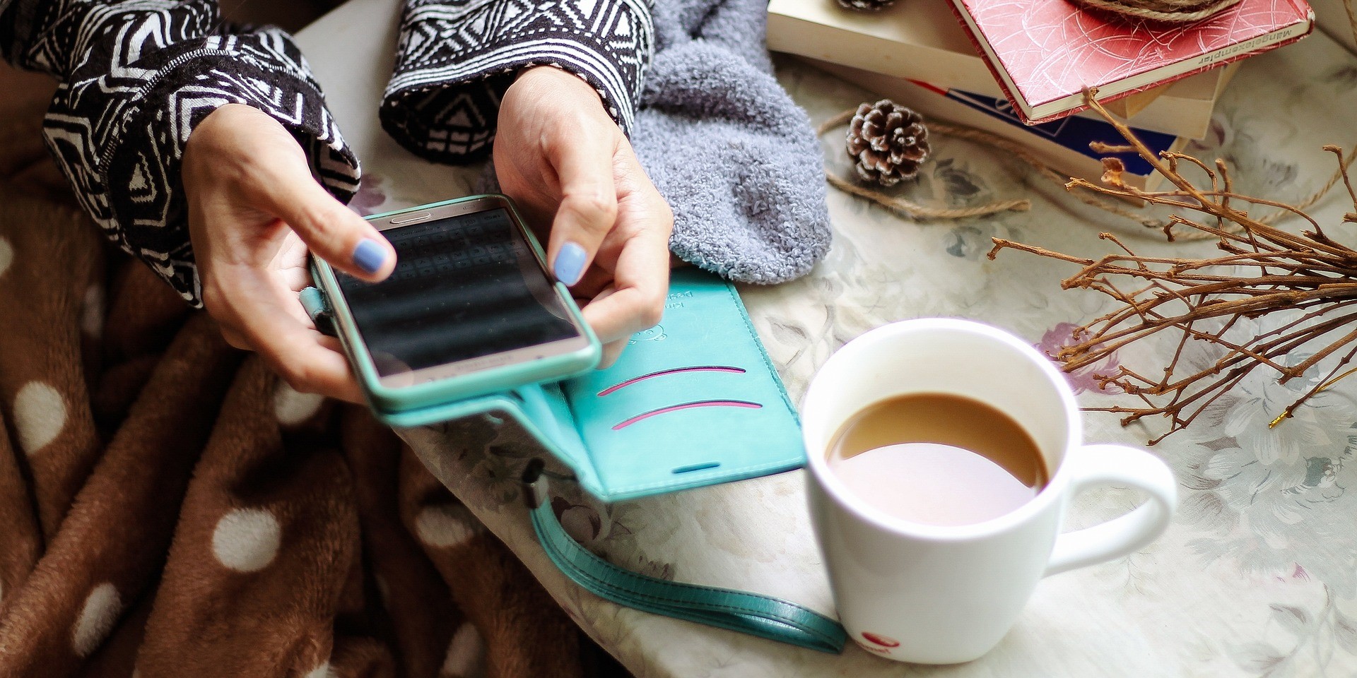 Eine Frau tippt an einem Smartphone und hat eine Tasse Kaffee vor sich stehen. Man sieht nur die Hände.