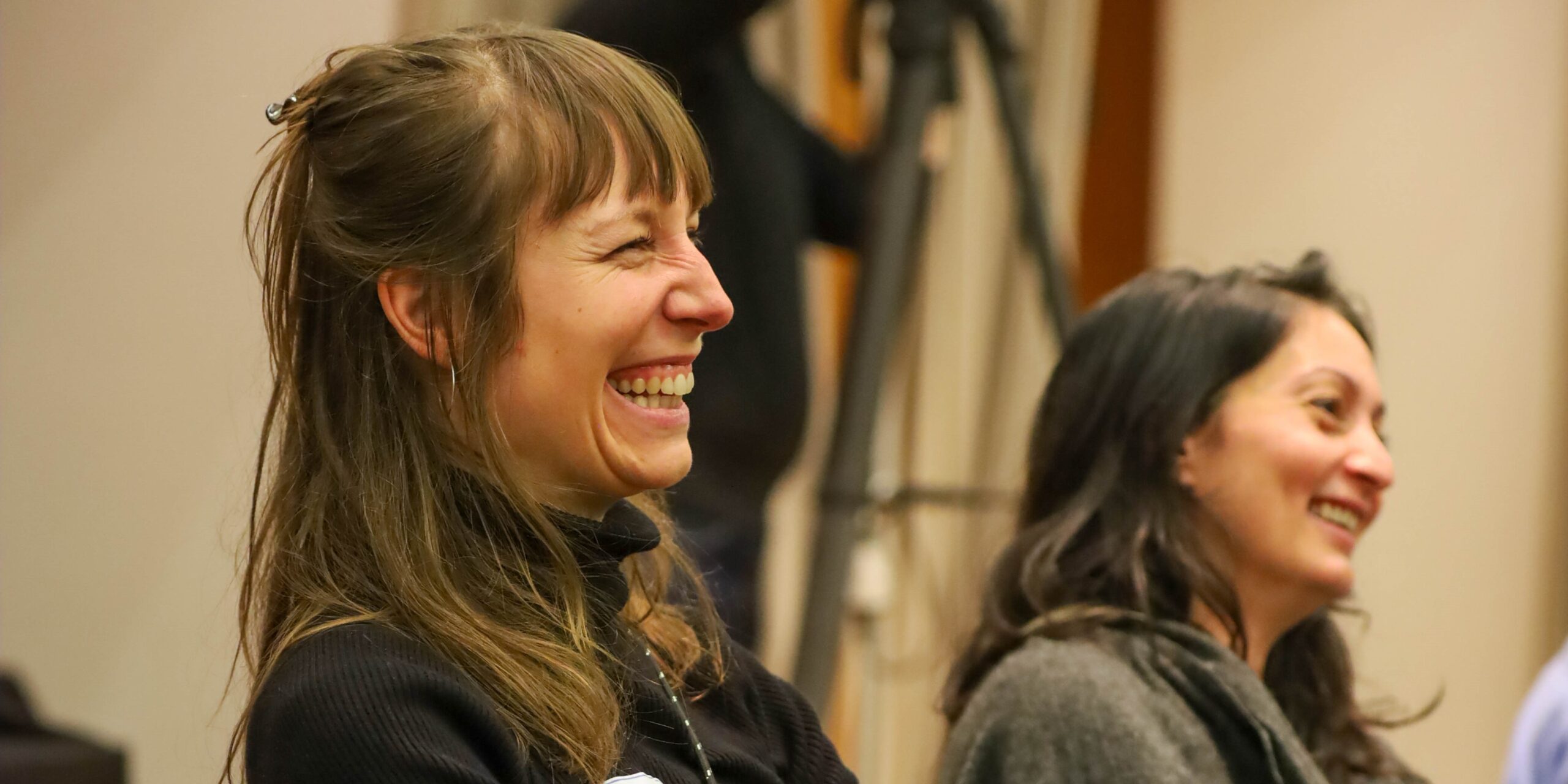 Zwei junge Frauen auf einer Veranstaltung die über einen Beitrag lachen und glücklich aussehen.