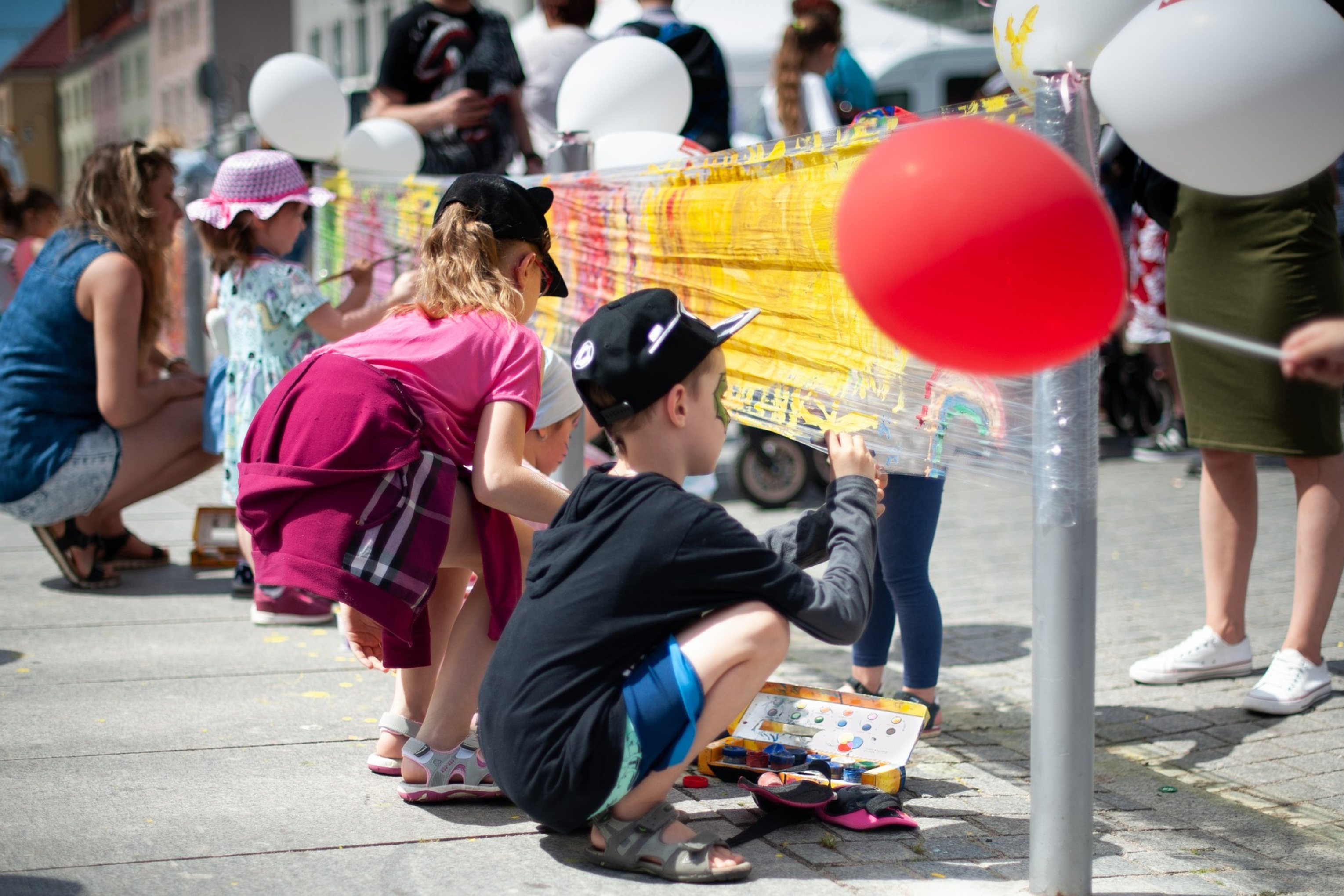 Kindern malen auf einem Straßenfest eine Straßensperre bunt an.