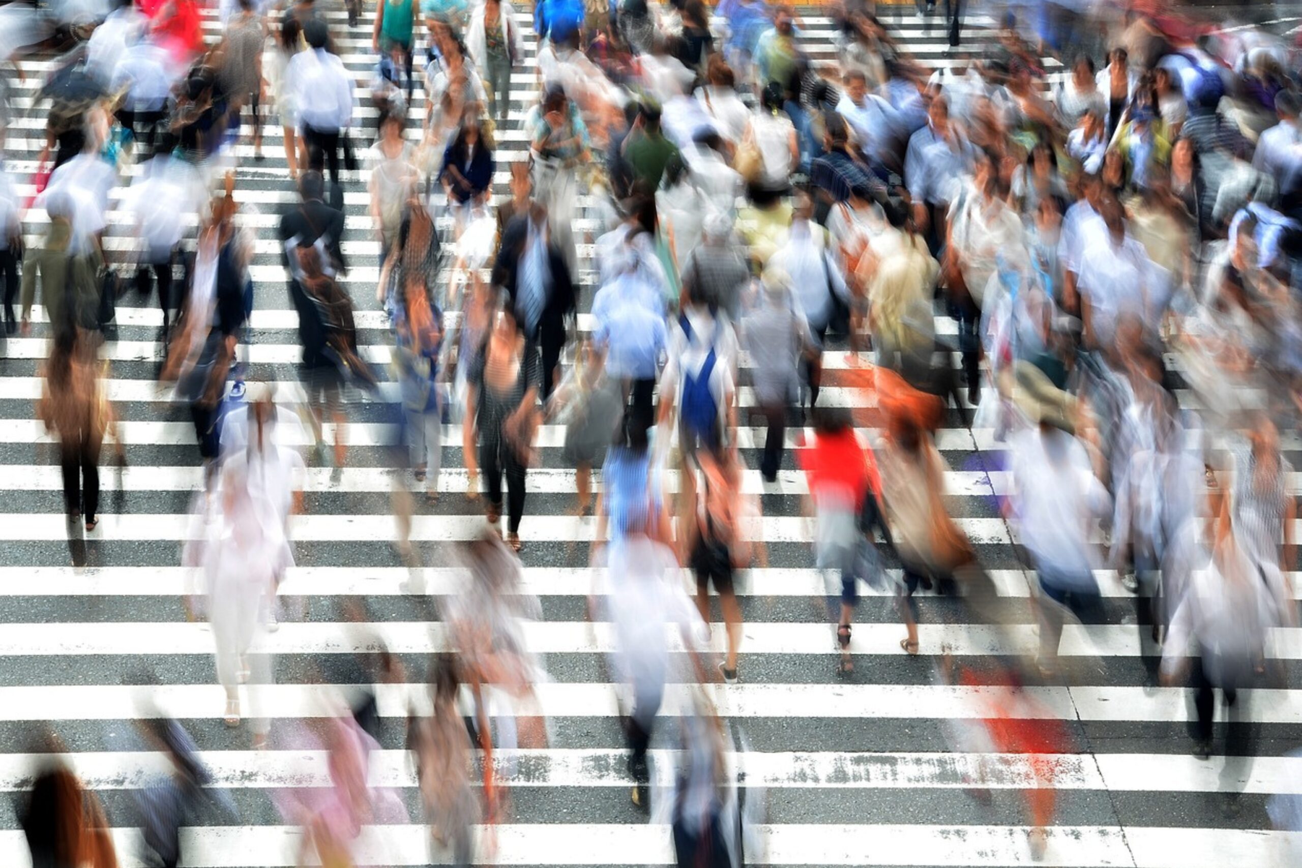 Verschwommene Silhouetten von Menschen die über einen sehr breiten Zebrastreifen gehen.