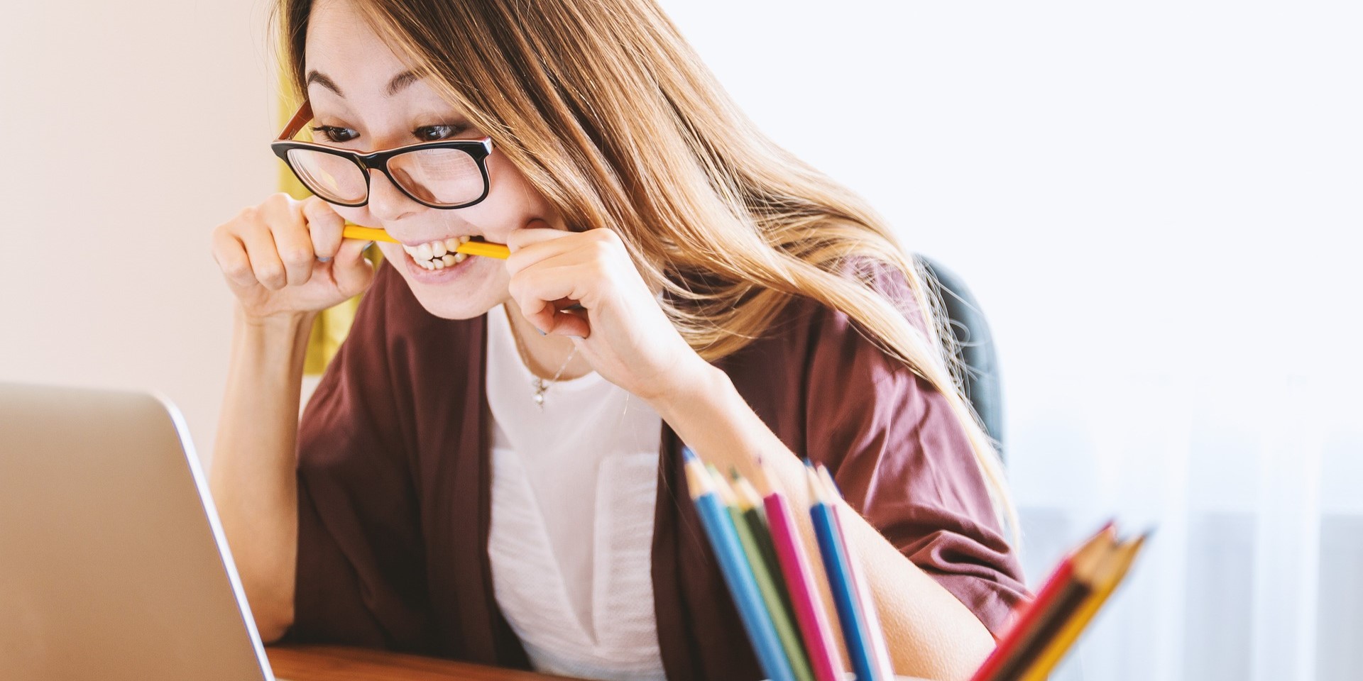 Eine junge Frau sitzt konzentriert vor ihrem Laptop und beißt auf einen Buntstift.