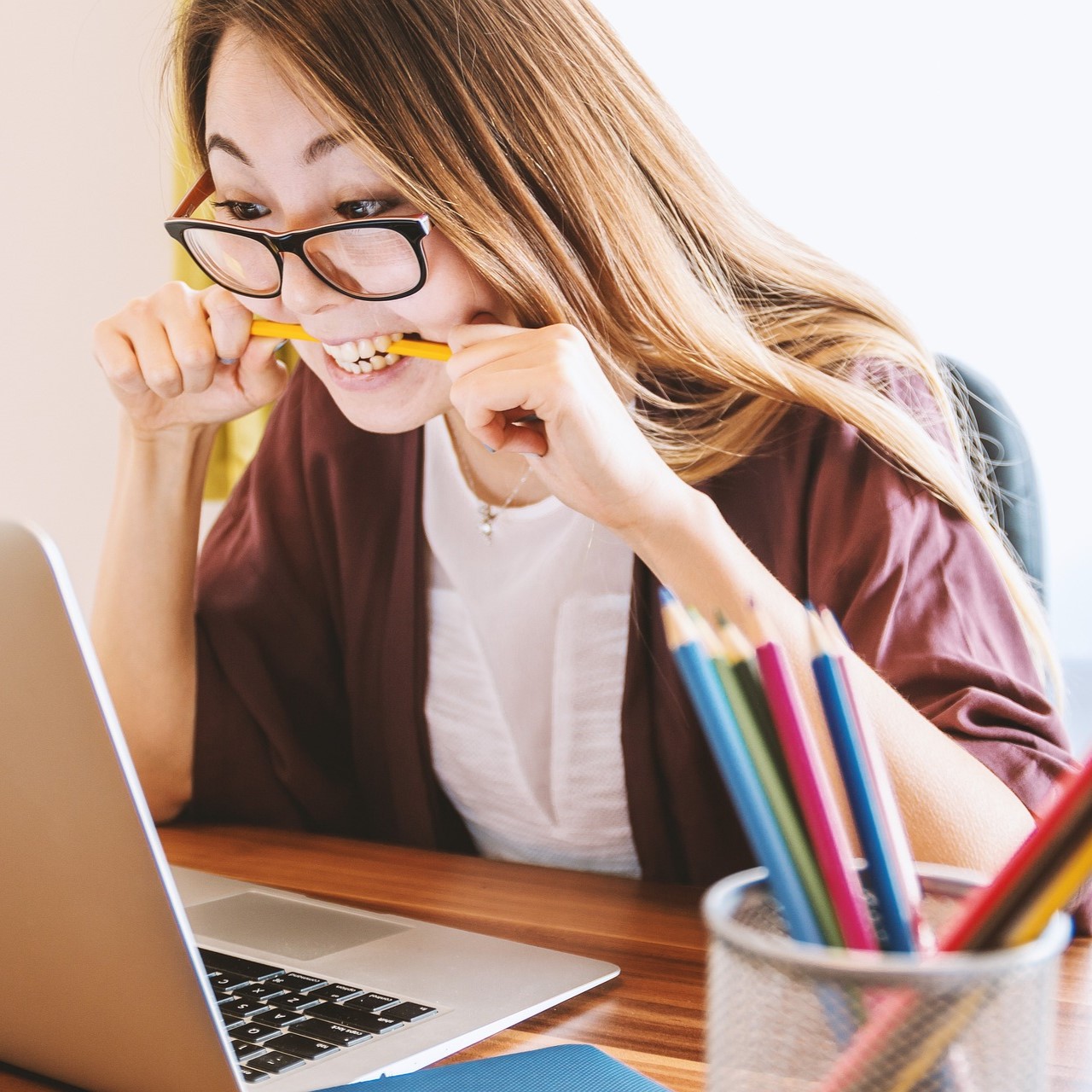 Eine junge Frau sitzt konzentriert vor ihrem Laptop und beißt auf einen Buntstift.