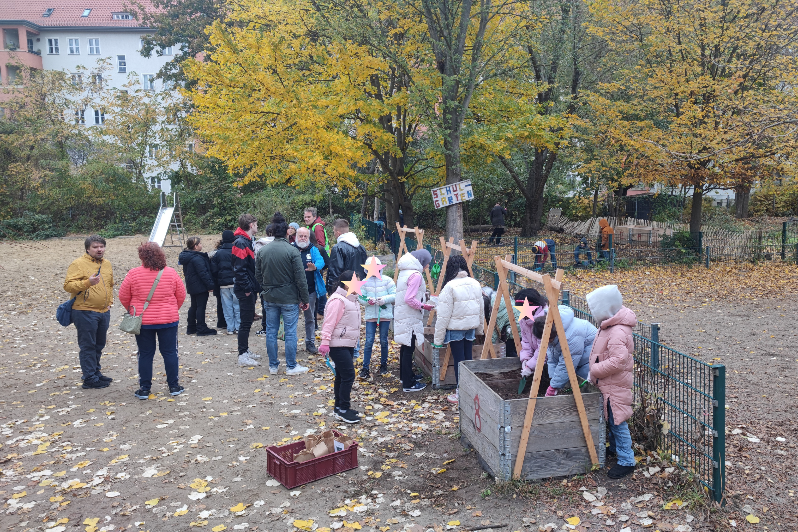 Ein Schulhof mit rund zwie Dutzend Erwachsenen und Kindern, die in Teilen in Hochbeeten gärtnern und sich unterhalten.