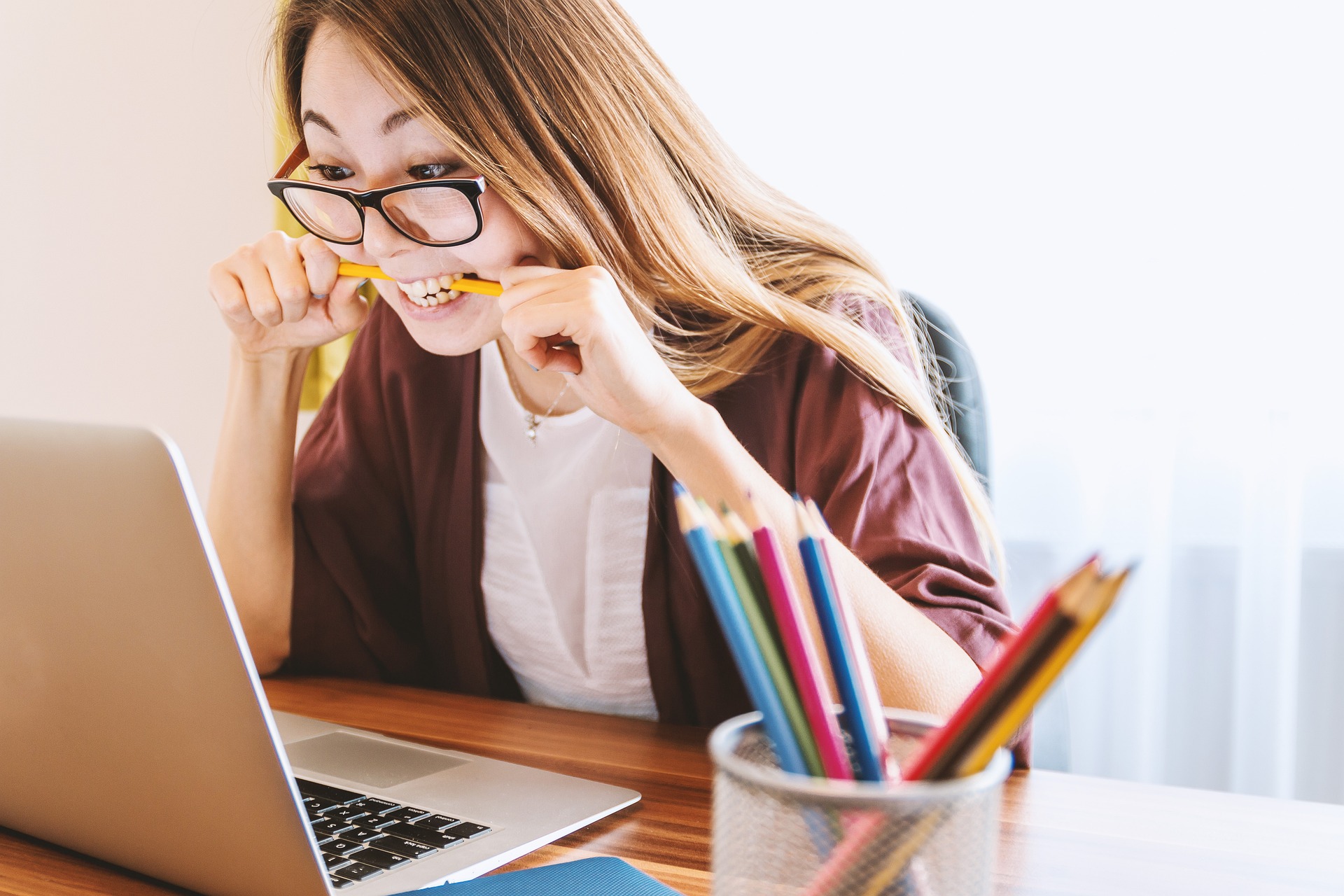 Eine junge Frau sitzt konzentriert vor ihrem Laptop und beißt auf einen Buntstift.