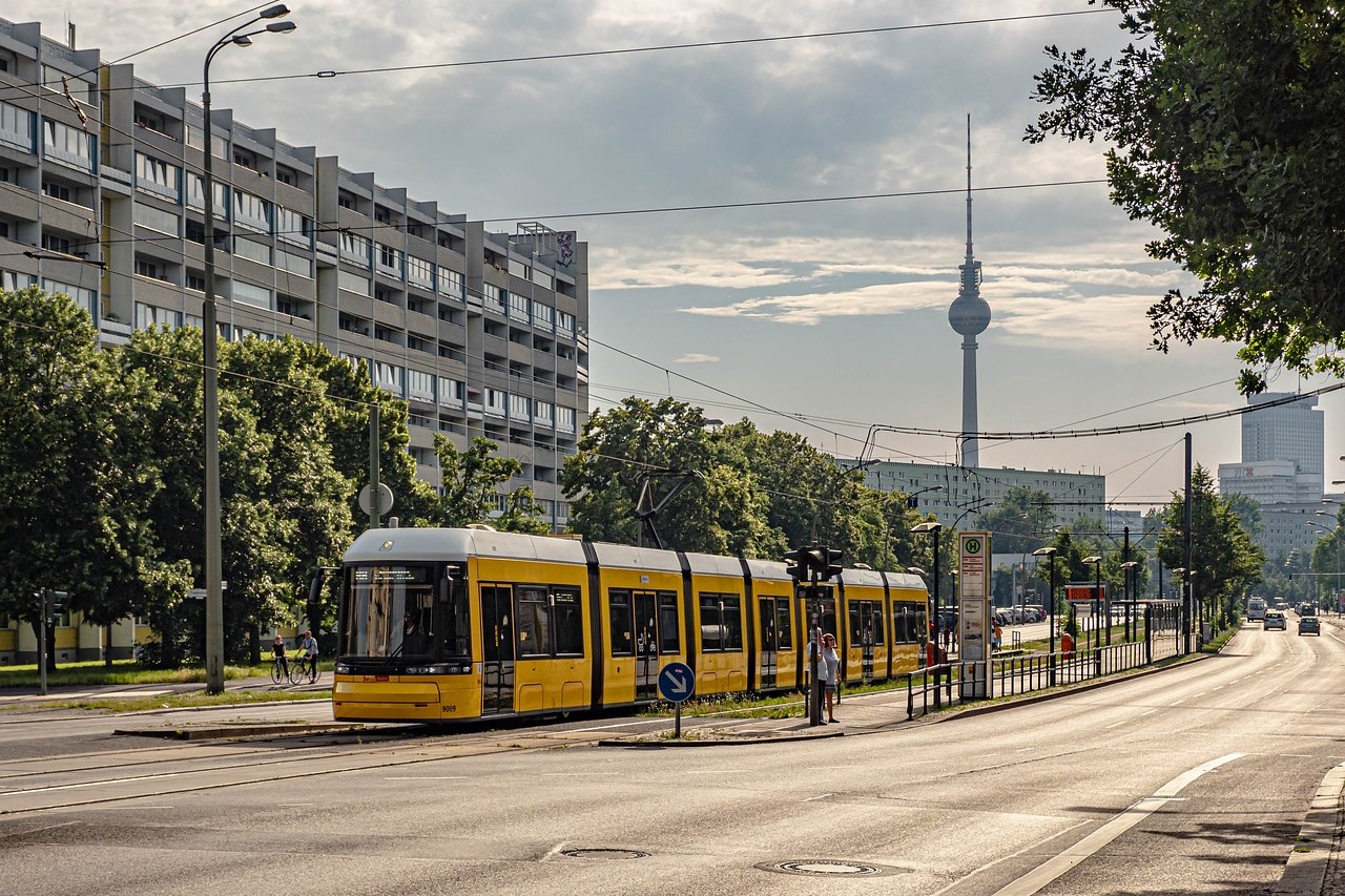 Eine Straße in Berlin mit einer Straßenbahn. Im Hintergrund ist der Fernsehturm zu sehen.